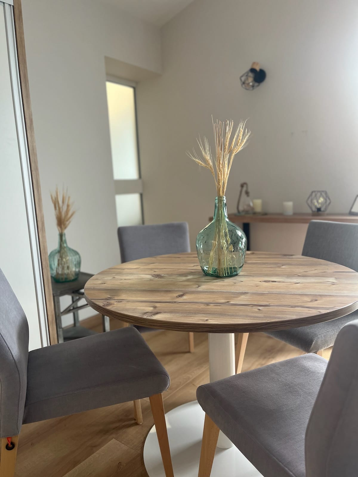 Table en bois avec vase et chaises grises.
